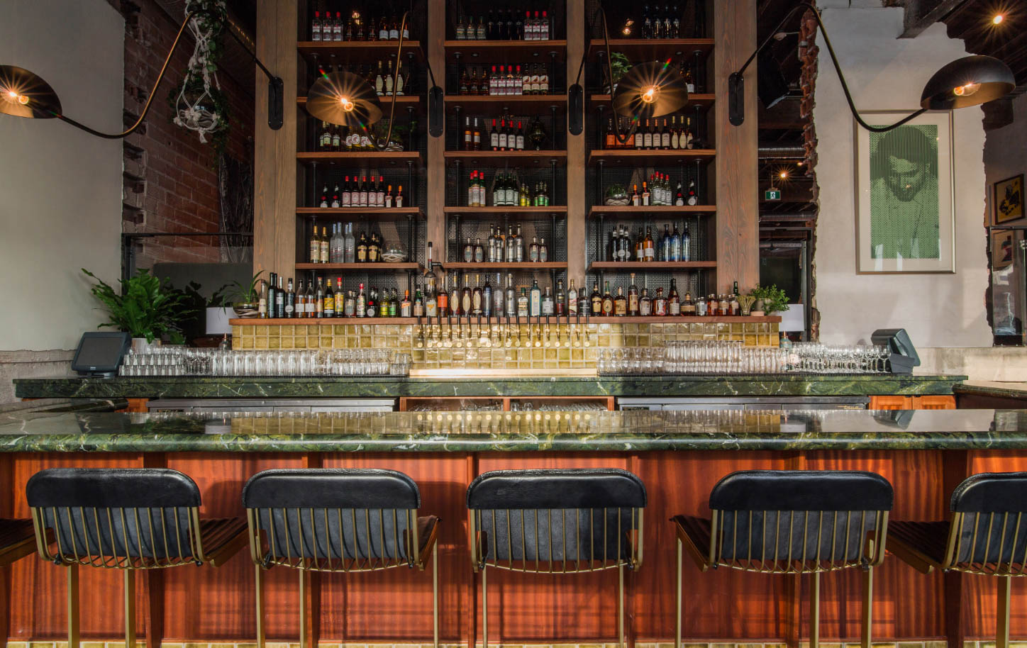 Gold and black bar chairs facing a green bar with a tall liquor wall in background
