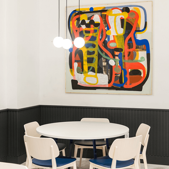 White and blue chairs surrounding round white dining table with colourful painting on the wall