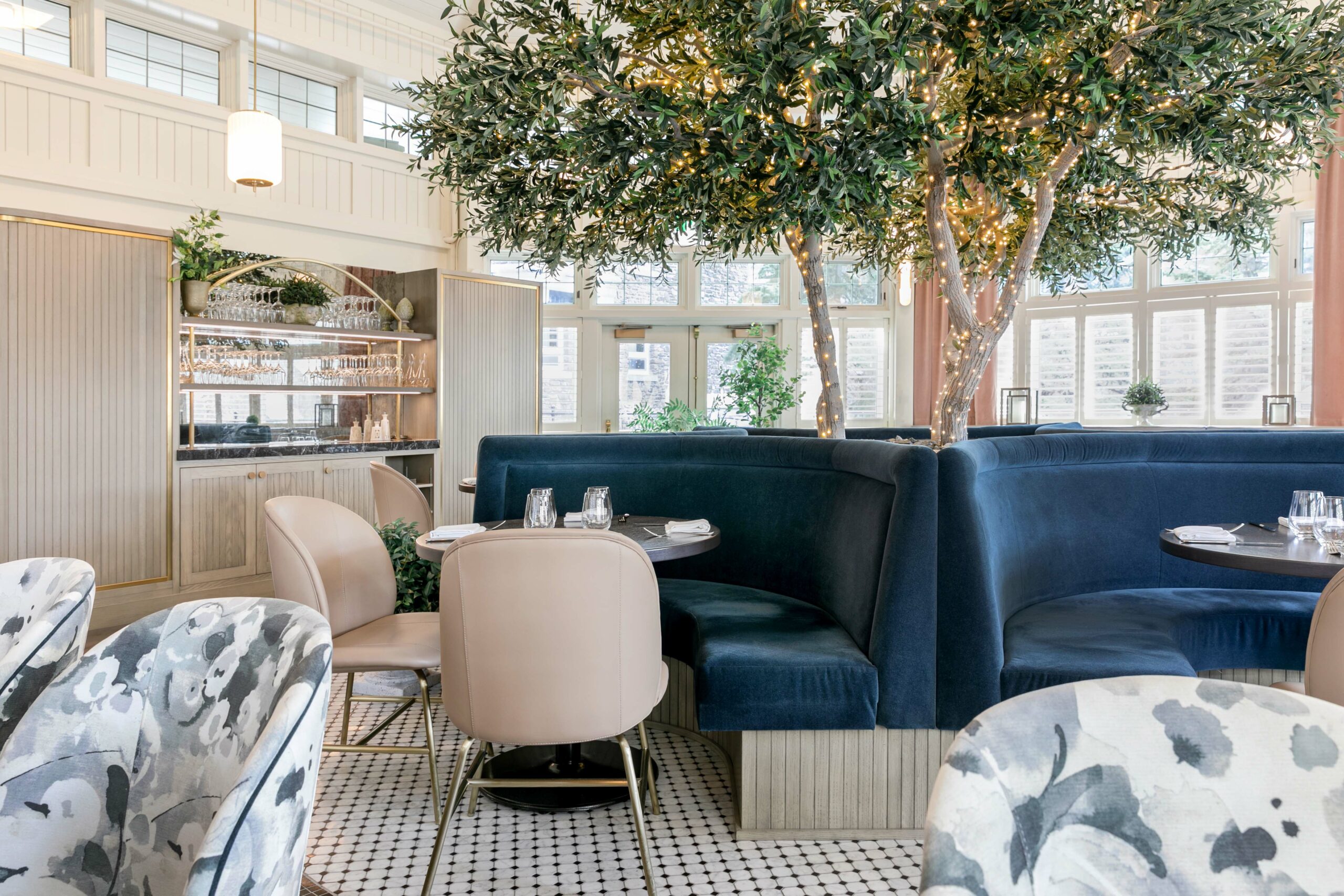 A dining area with blue velvet seating booths and a tree wrapped in lights in the middle