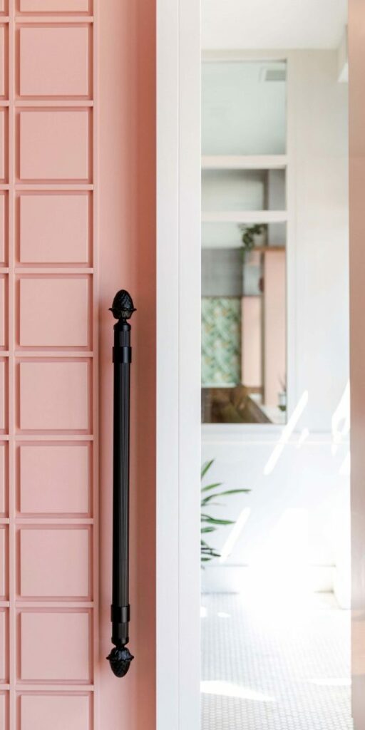 Light pink door with a black handle next to a hallway