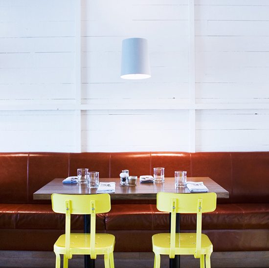 Neon yellow chairs facing wooden table and long leather seating bench against a white wood paneled wall