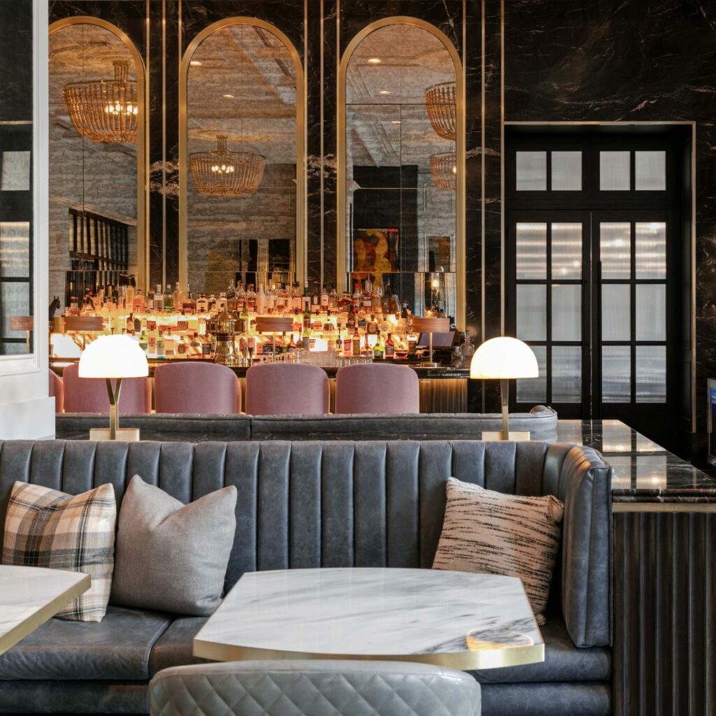 Marble table and grey seating bench in the foreground with a large restaurant bar filled with liquor in the background