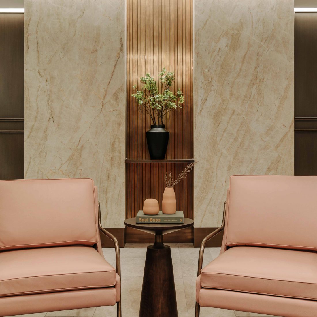 Pink chairs are on either side of a small coffee table stacked with a book and vases