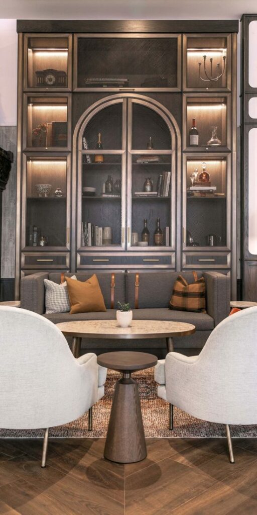 Low white chairs facing a coffee table, grey couch with pillows, and a big shelving unit filled with trinkets