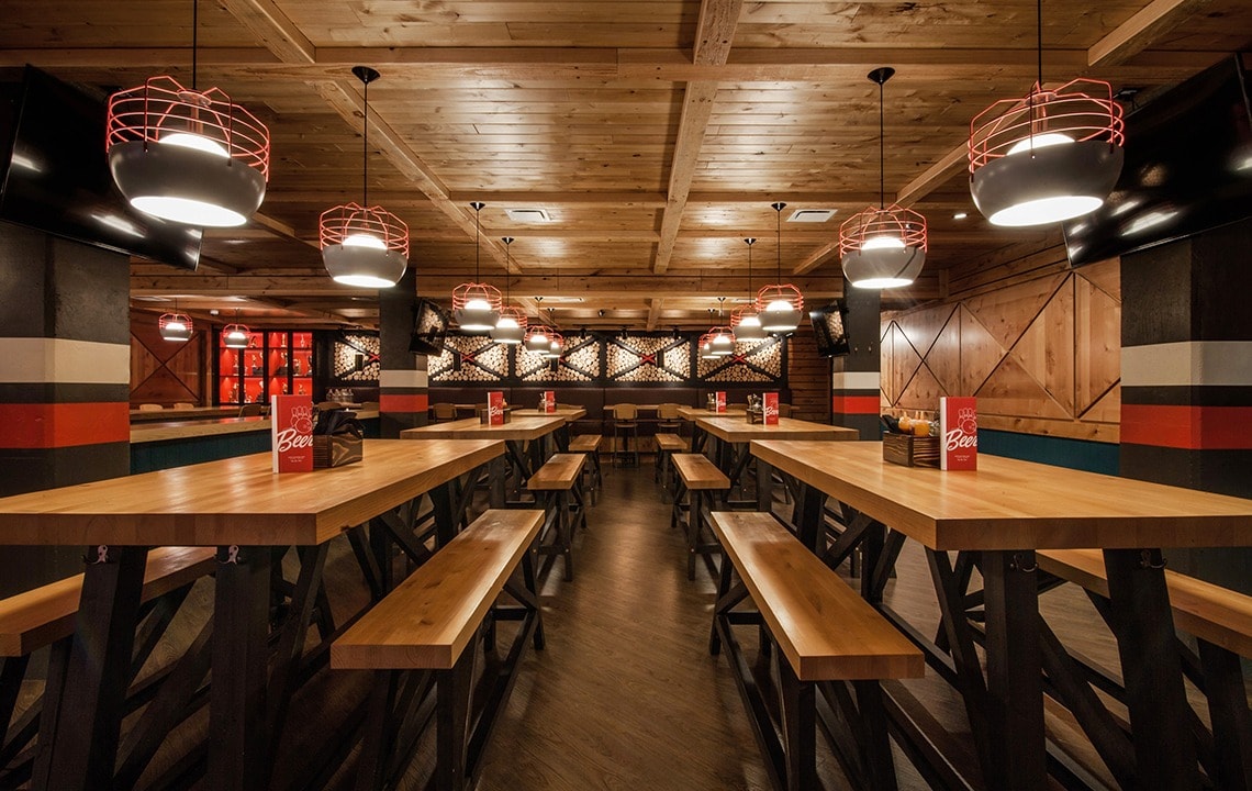 Wooden tables and seating benches throughout are below a wooden ceiling that has black and red light fixtures hanging