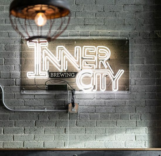 A neon sign that says Inner City Brewiing against a grey brick wall