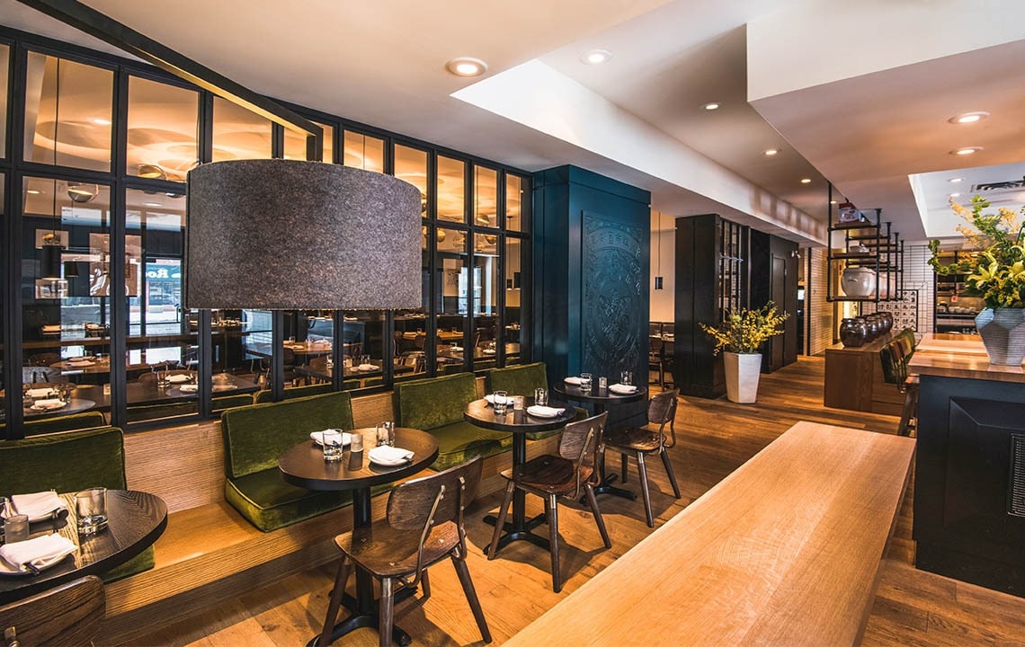 Brown chairs facing brown tables with green seating booths facing the chairs and tables, glass divider in background