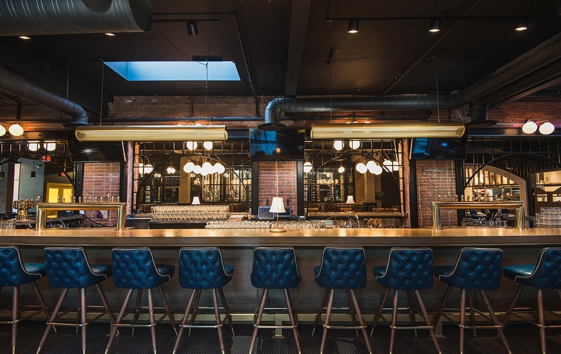 Dark blue bar chairs facing a gold bar top with exposed ceilings above