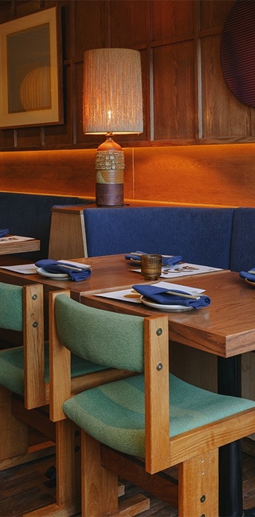 Green and brown chairs facing set dining tables and dark blue seating bench with a lamp between tables
