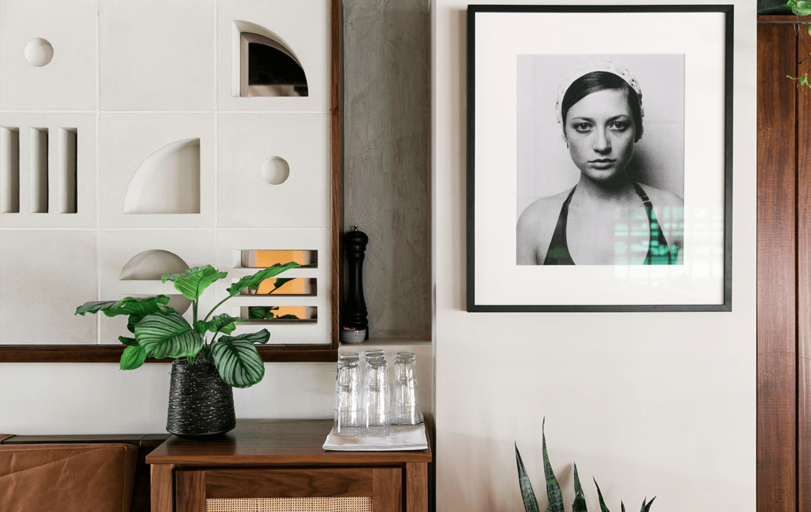 A portrait of a woman is to the right of art decor and a plant and glasses on top of a table