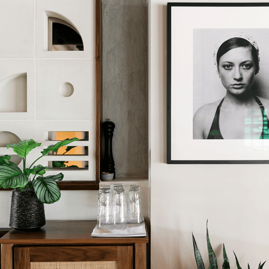 A portrait of a woman is to the right of art decor and a plant and glasses on top of a table