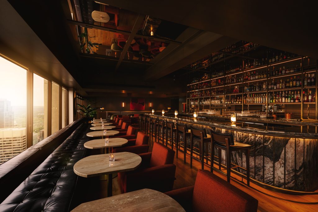 Fabric red chairs facing dining tables, long black leather seating bench, and windows to the left, large bar with liquor filled shelves to the right