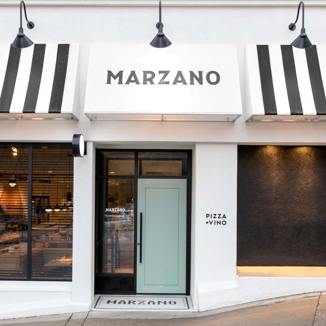 Black and white awnings hanging above a window and teal blue door, middle awning say Marzano
