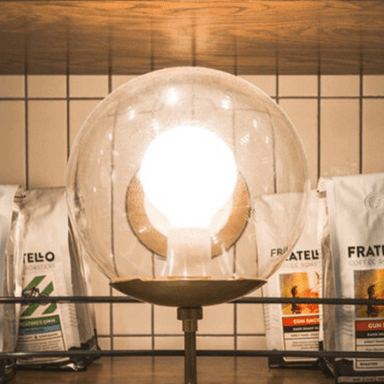 A globe shaped lamp is in front of a shelf that has coffee bags sitting on it