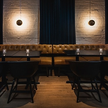 Chairs facing tables and a tan leather seating bench are in the foreground and a bar with red bar stools are in the background