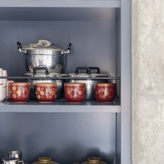 Red and gold cups, and silver pots are stacked in a grey shelving unit