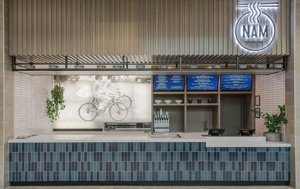 A blue tiled food counter is in front of an illustration of people biking that is next to menus on a screen