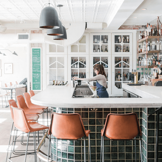 A woman is making a cocktail at a white and green tiled bar top