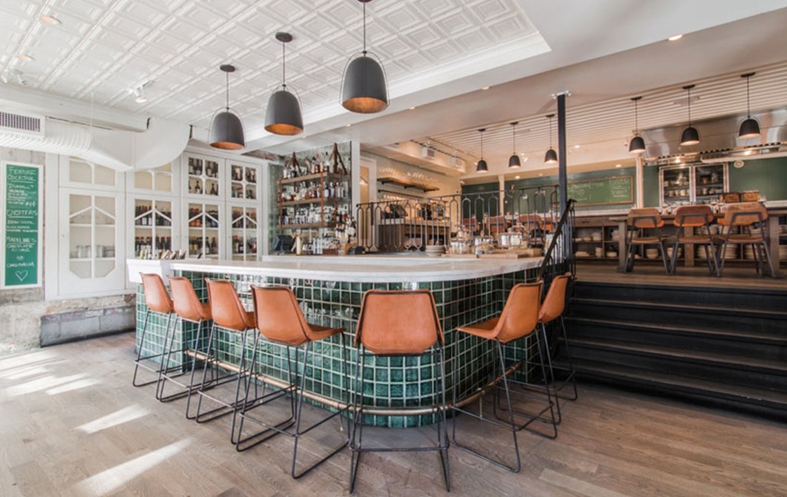 Brown leather bar stools sit under an L-shaped bar top with stairs to the right