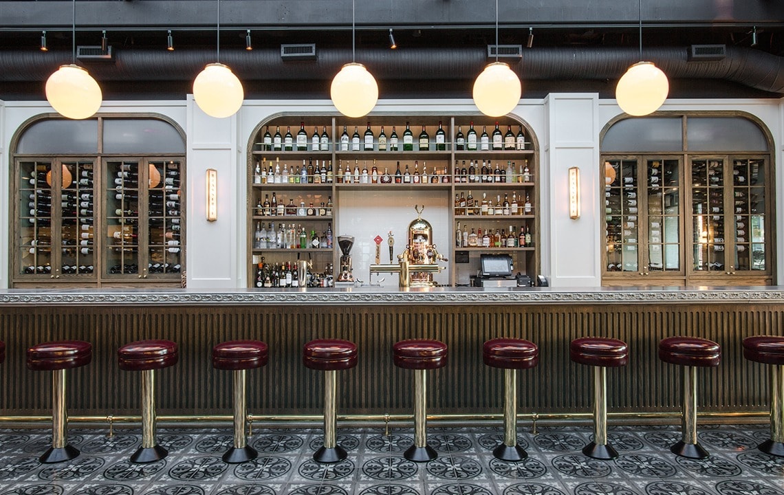 Gold and red bar stools underneath a long bar top facing a bar with liquor filled shelves