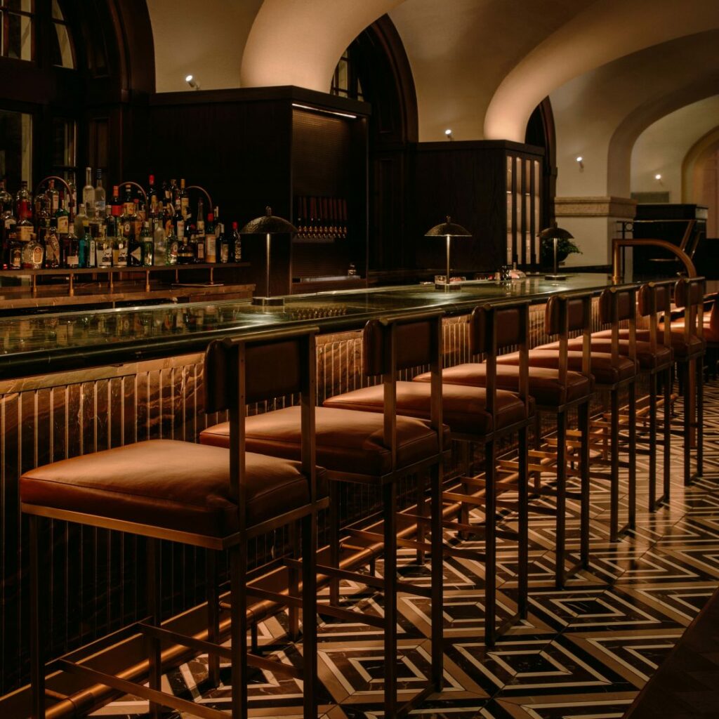 Bar chairs sit under a long bar counter on top of a patterened tile floor