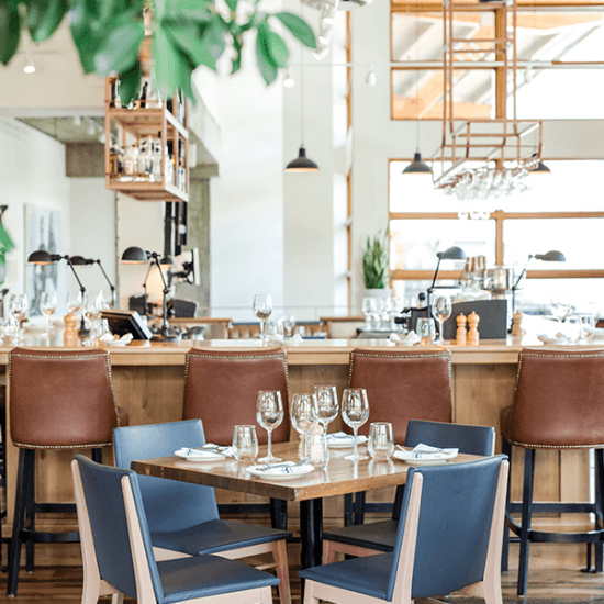 Blue chairs surrounding a set dining table with a bar in the background surrounded by brown bar chairs