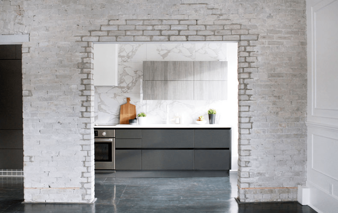 A white weathered brick archway that leads to a kitchen facing cupboards, cabinets and stove