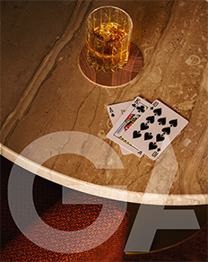 Playing cards and a glass of scotch are on top of a tan marble table