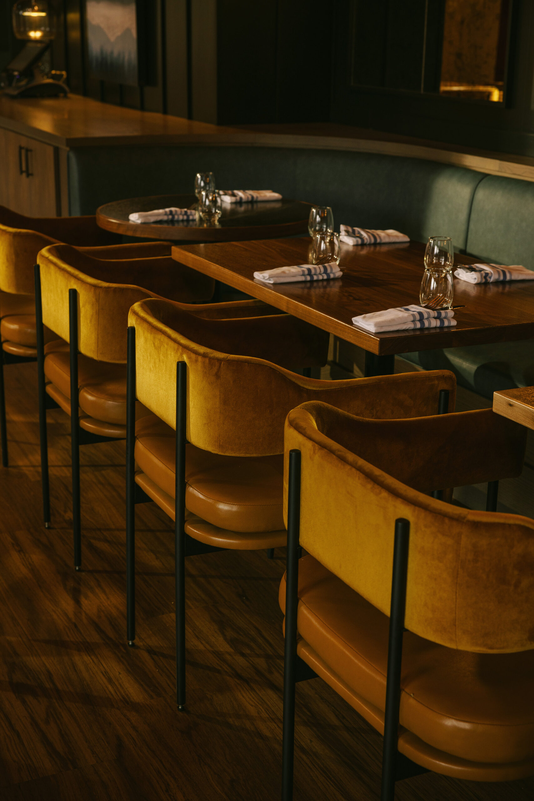 Four dark yellow chairs are featured in a line, facing a green banquette with warm wooden tables in between.
